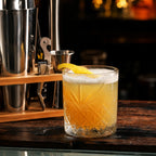 Close-up of a finished cocktail with ice and garnish beside the RüK stainless steel cocktail shaker set.