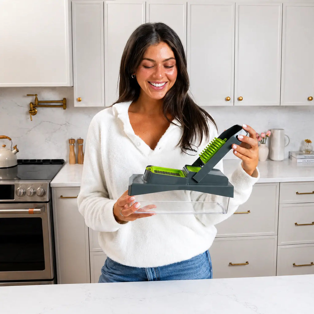 A woman holding the RüK multifunctional vegetable chopper and mandoline slicer in a modern Scandinavian-style minimalist kitchen, featuring a premium lifestyle aesthetic, completely dishwasher safe.